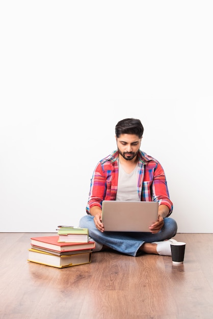 Étudiant d'université ou d'université asiatique indien assis avec un ordinateur portable avec des livres sur un plancher en bois sur fond blanc