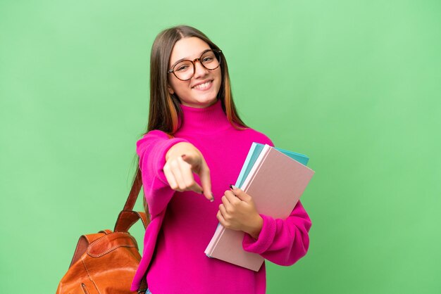 Étudiante adolescente caucasienne sur fond isolé pointant vers l'avant avec une expression heureuse