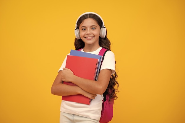 Étudiante adolescente avec des écouteurs et des livres sur un fond de studio isolé Enfants d'école avec un sac à dos