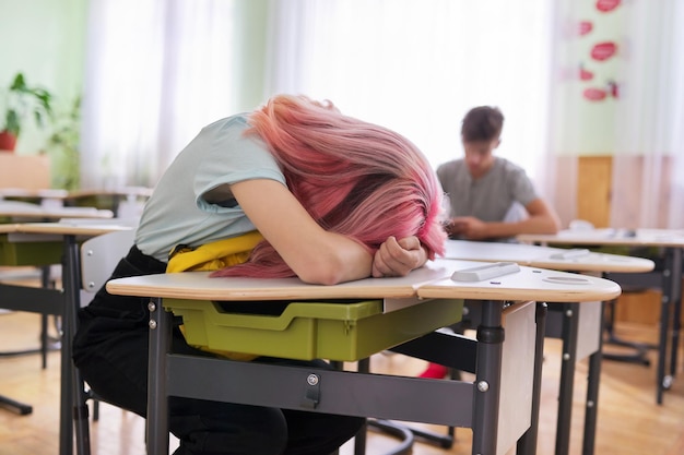 Étudiante adolescente fatiguée endormie sur son bureau. La fille a mis sa tête sur un sac à dos, fond de classe