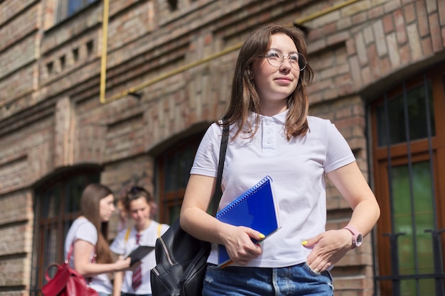 Étudiante adolescente fille posant en plein air en T-shirt blanc. Bâtiment en brique de fond, groupe d'étudiantes. Début des cours, retour au collège, espace copie