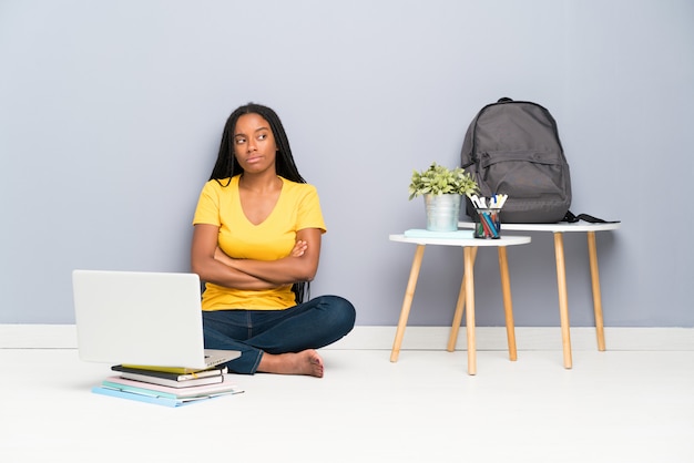 Étudiante afro-américaine étudiante avec de longs cheveux tressés, assise sur le sol, pensant à une idée