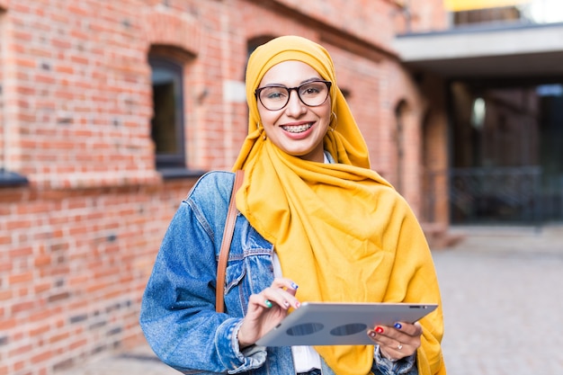 Étudiante arabe. Belle étudiante musulmane portant un hijab jaune vif tenant une tablette.