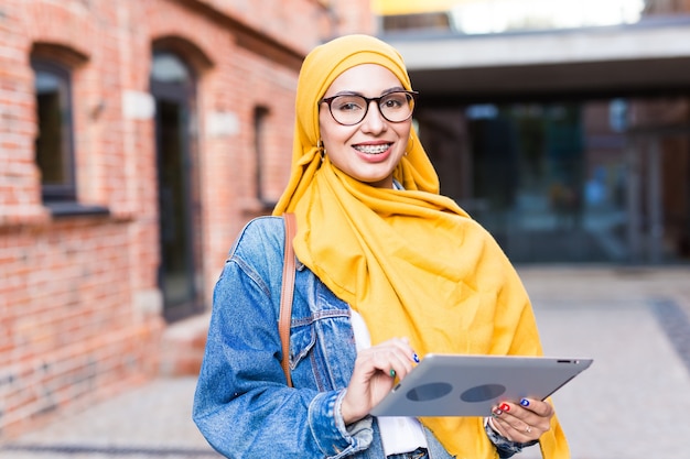 Étudiante arabe. Belle étudiante musulmane portant un hijab jaune vif tenant une tablette.