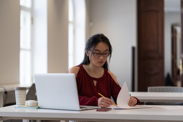 Étudiante asiatique concentrée se préparant à l'examen ou faisant ses devoirs dans la salle de lecture de l'université