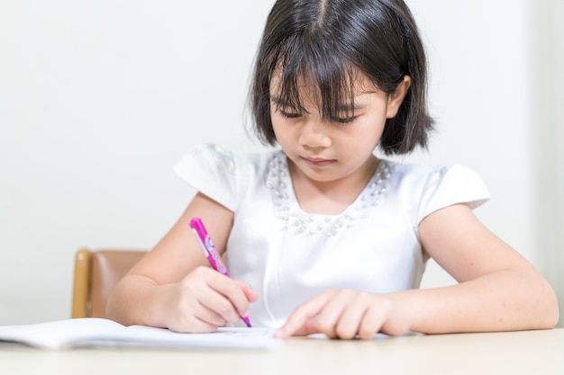 Étudiante asiatique d'enfants de petite fille écrivant sur le cahier faisant des devoirs et l'auto-étude à la maison