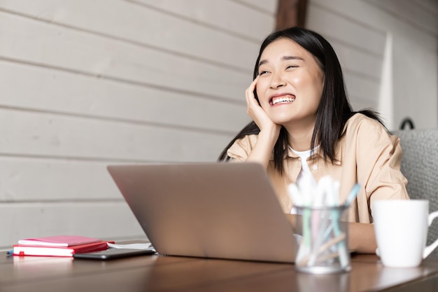 Étudiante asiatique travaillant sur un ordinateur portable en riant et en souriant parlant à quelqu'un qui étudie ensemble de ...