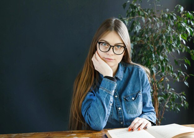 Étudiante aux cheveux longs portant des lunettes étudiant ou travaillant dans la classe à la table en bois