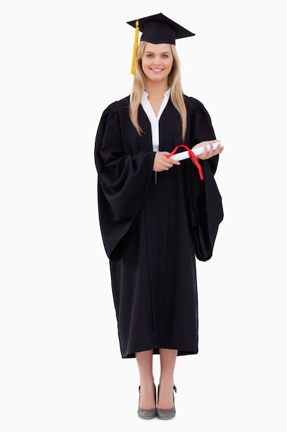 Étudiante blonde souriante en robe de diplômé tenant son diplôme