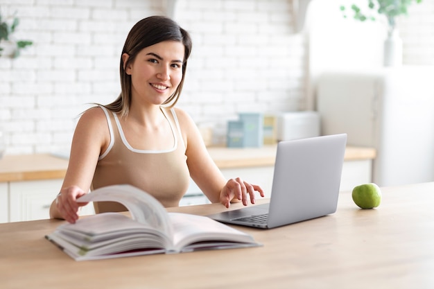 Étudiante caucasienne belle jeune femme regardant un cours vidéo de webinaire ou étudiant en ligne assis à la maison dans la cuisine, concept d'apprentissage électronique