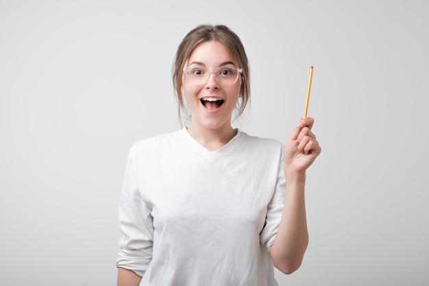 Étudiante caucasienne à lunettes et t-shirt blanc pointant une idée