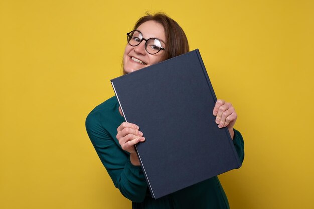 Étudiante ou enseignante de race blanche dans des verres souriant, tenant des livres et regardant la caméra. Prise de vue en studio