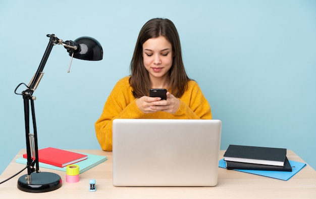 Étudiante étudie dans sa maison sur le mur bleu en envoyant un message avec le mobile