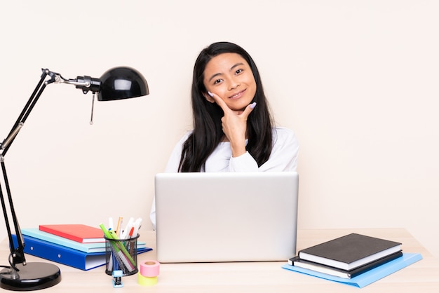 Étudiante fille asiatique dans un lieu de travail avec un ordinateur portable isolé sur un mur beige souriant