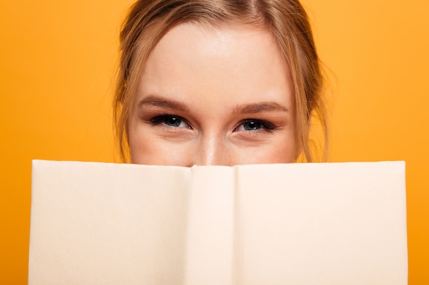 Étudiante heureuse jeune femme couvrant le visage avec le livre