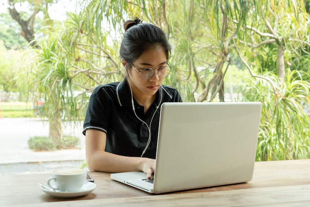 Étudiante jeune femme asiatique travaillant sur ordinateur portable avec écouteur au café.