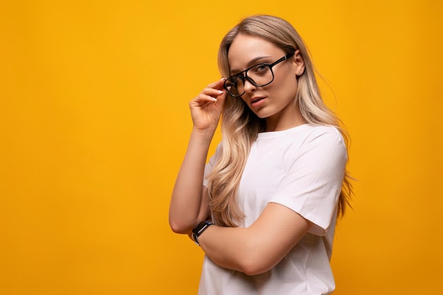 Étudiante à lunettes et un t-shirt blanc sur fond jaune studio