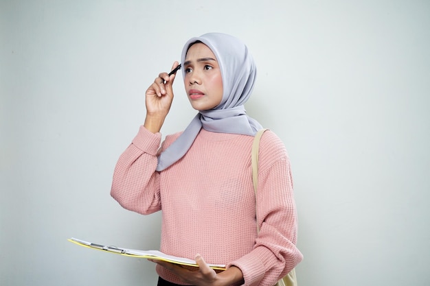 Étudiante musulmane asiatique souriante en pull rose avec sac tenant une planche et pointant une planche vide