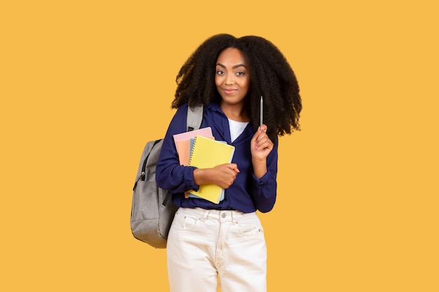 Étudiante noire confiante avec un sac à dos et des cahiers sur fond jaune