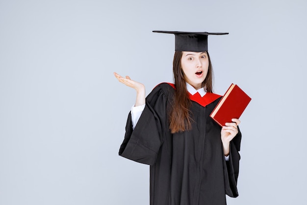 Étudiante en robe académique tenant un livre rouge. photo de haute qualité