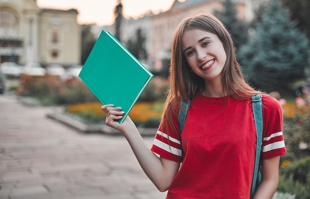 Étudiante en t-shirt rouge avec un sac à dos tenant un bloc-notes et souriant