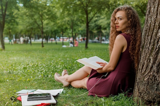 Étudiante tenant un livre et assise sous un arbre