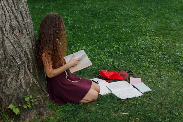 Étudiante tenant un livre et assise sous un arbre