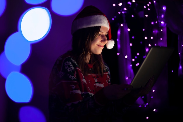 Étudiante en vêtements de Noël est assise à la maison avec un ordinateur portable la nuit