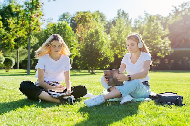 Étudiantes adolescentes assises sur une pelouse verte dans le parc avec sac à dos, livres, tablette numérique, boire une bouteille d'eau. Université, collège, école, éducation et connaissances, mode de vie des adolescents