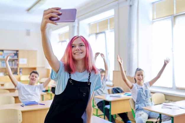 Étudiants adolescents s'amusant dans la salle de classe, fille à la mode brillante prenant une photo de selfie avec un groupe d'amis de camarades de classe à l'école