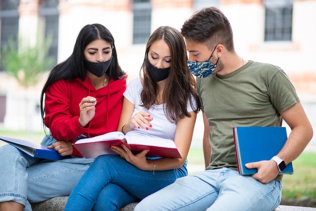 Étudiants étudiant ensemble assis sur un banc à l'extérieur et portant des masques pendant les périodes de coronavirus