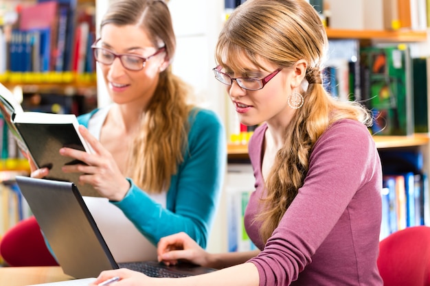 Étudiants - jeunes femmes en bibliothèque avec ordinateur portable et livre d'apprentissage en groupe