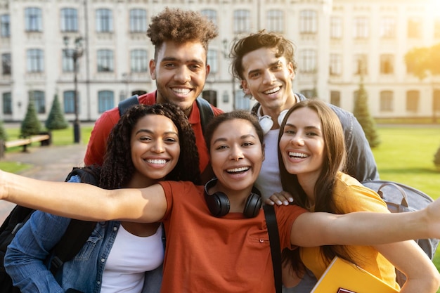 Étudiants multiculturels joyeux posant ensemble faisant du selfie sur le campus universitaire à l'extérieur