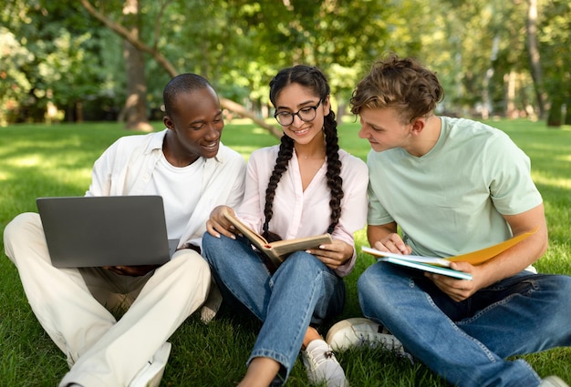 Étudiants multiraciaux amis apprenant ensemble à lire des livres et à utiliser un ordinateur portable assis dans