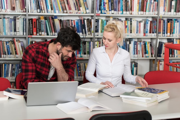 Étudiants préparant l'examen et apprenant des leçons dans la bibliothèque de l'école faisant des recherches sur un ordinateur portable et naviguant sur Internet dans la bibliothèque