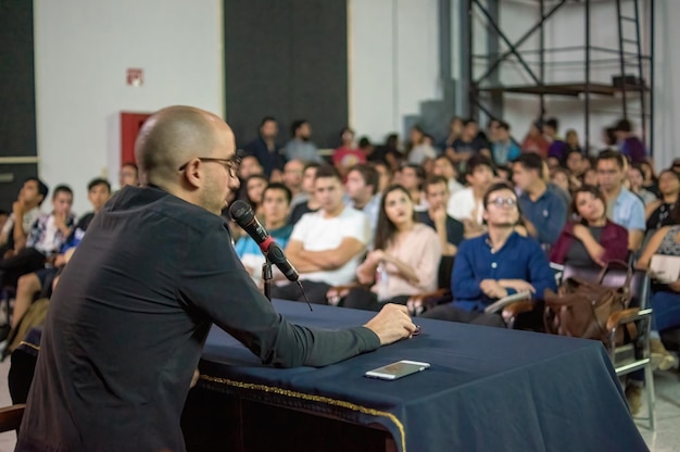 Étudiants prêtant attention à une conférence donnée par une femme projetant sur les livres et l'éducation architecturale