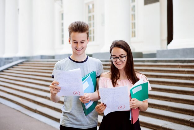 Étudiants souriants avec les résultats des tests près du bâtiment de l'université