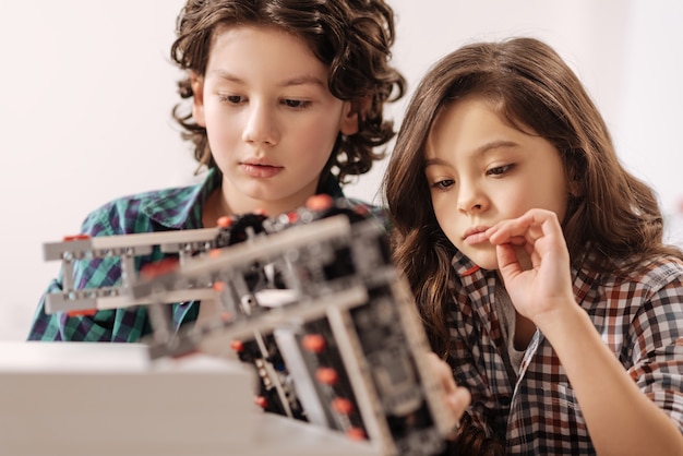 Étudier un sujet scientifique. Enfants concentrés et réfléchis positifs assis dans la classe de sciences et utilisant un gadget tout en exprimant leur intérêt