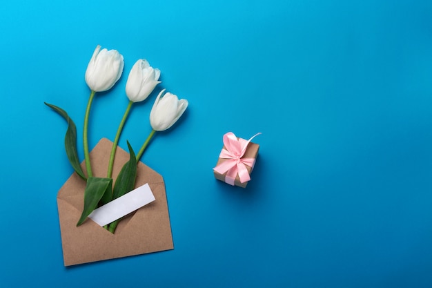 Tulipes blanches avec boîte-cadeau, une note d&#39;amour et une enveloppe sur un fond bleu