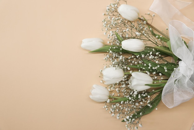 Tulipes blanches et bouquet de fleurs de gypsophile sur fond beige Concept de célébration d'anniversaire de la fête des mères Copier l'espace pour la maquette de texte