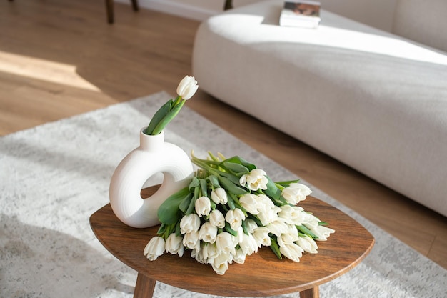 Des tulipes blanches dans un vase moderne sur une table en bois avec un canapé en arrière-plan