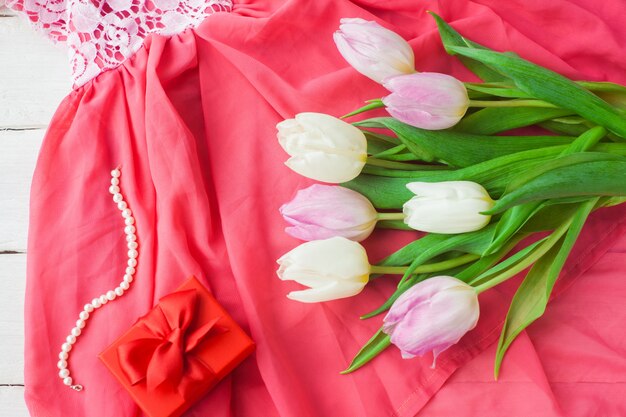 Tulipes blanches et violettes et un cadeau dans une boîte rouge sur un fond en bois blanc