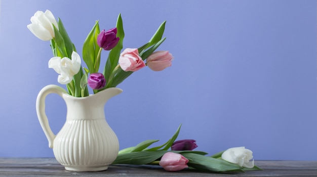 Tulipes en cruche sur surface violette