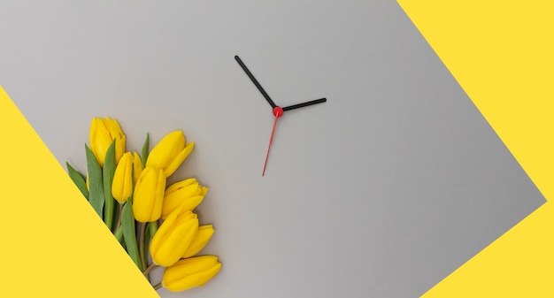 Tulipes jaunes et aiguilles d'horloge sur fond jaune et gris