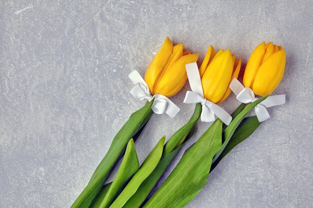 Tulipes jaunes avec des arcs blancs sur un fond de béton gris clair Concept de carte de voeux Vue de dessus avec copie espace Mise à plat