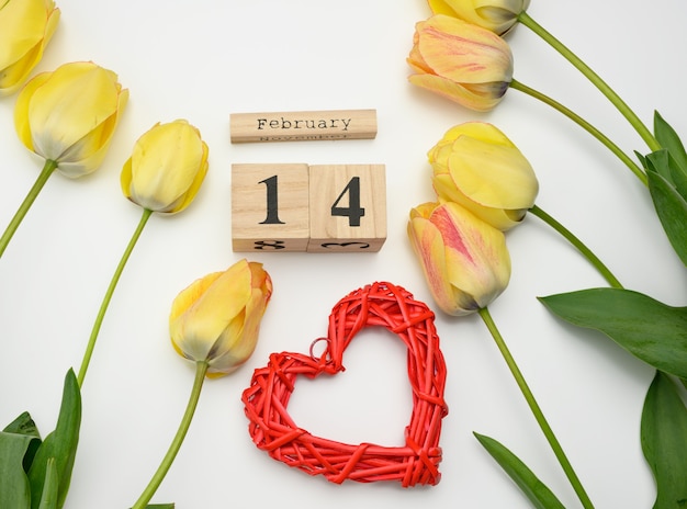 Photo tulipes jaunes, calendrier en bois avec date du 14 février et coeur rouge sur surface blanche, vue du dessus