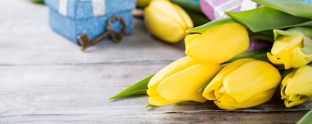 Tulipes jaunes dans une boîte en métal bleu et coffrets cadeaux sur la surface gris clair. Carte de voeux pour la fête des mères. Copiez l'espace. Bannière