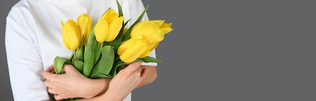 Tulipes jaunes dans les mains des femmes sur fond gris avec espace de copie Bannière festive pour le site Web Photo de haute qualité