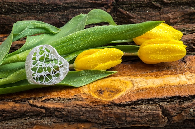 Tulipes jaunes fraîches avec des gouttes d'eau sur une planche de bois naturel.