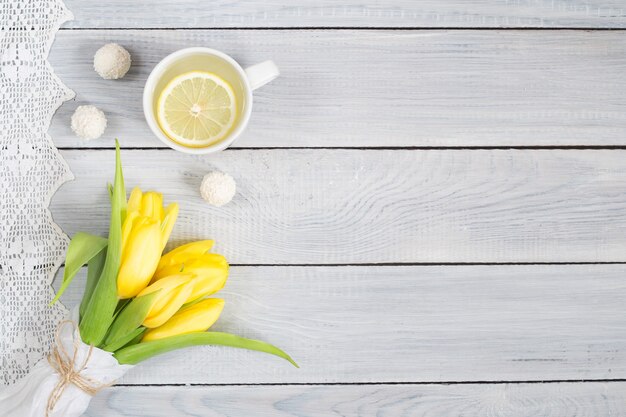 Tulipes jaunes, thé au citron et bonbons sur une table en bois blanche